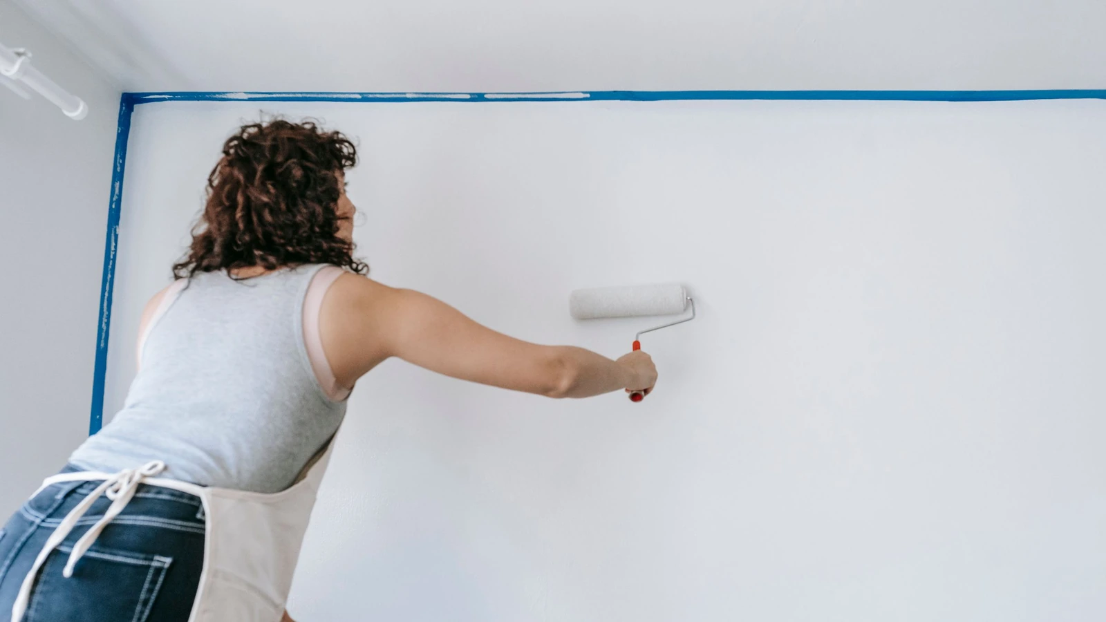 Peintre passant un rouleau sur un mur blanc protégé par un ruban de masquage